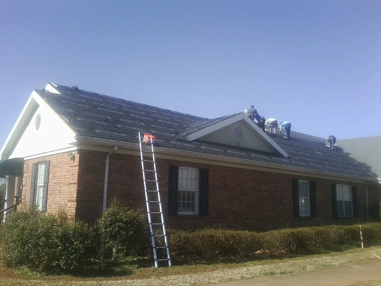 Crew tearing shingles off a brick ranch roof with a ladder set — Emergency Roof Repair work by our crew in Milmay