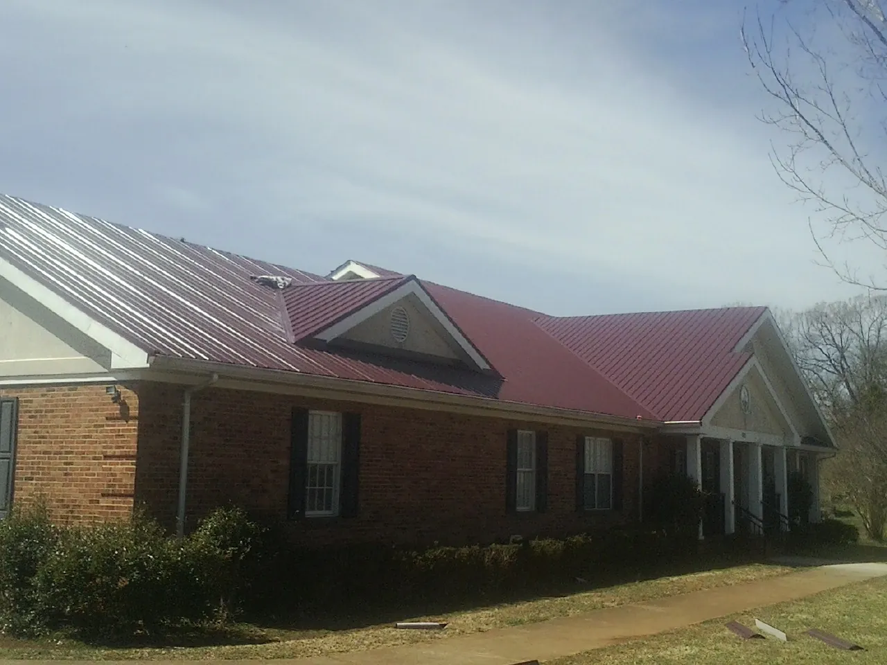 Red metal roof with gabled entries on a long brick building, from a Hail Damage Roof Repair job in Milmay