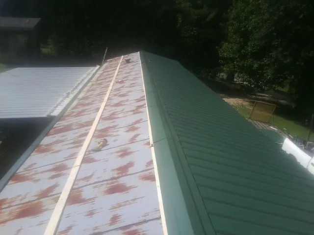 Old rusted panels beside newly installed green metal roofing — Wind Damage Roof Repair by Roofing Brothers in Milmay