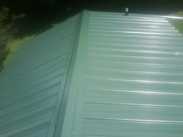 New green metal panels meeting at the ridge of a roof — Flat Roof Repair work by our crew in Milmay