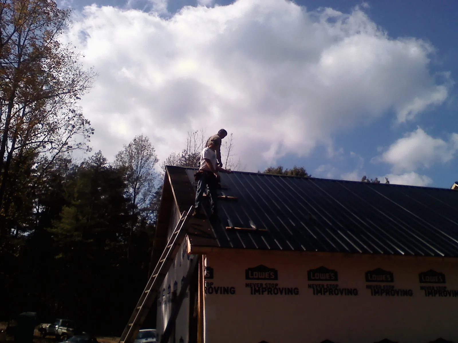 Roofer fastening dark metal panels high against a cloudy sky, from a Roof Inspection job in Milmay
