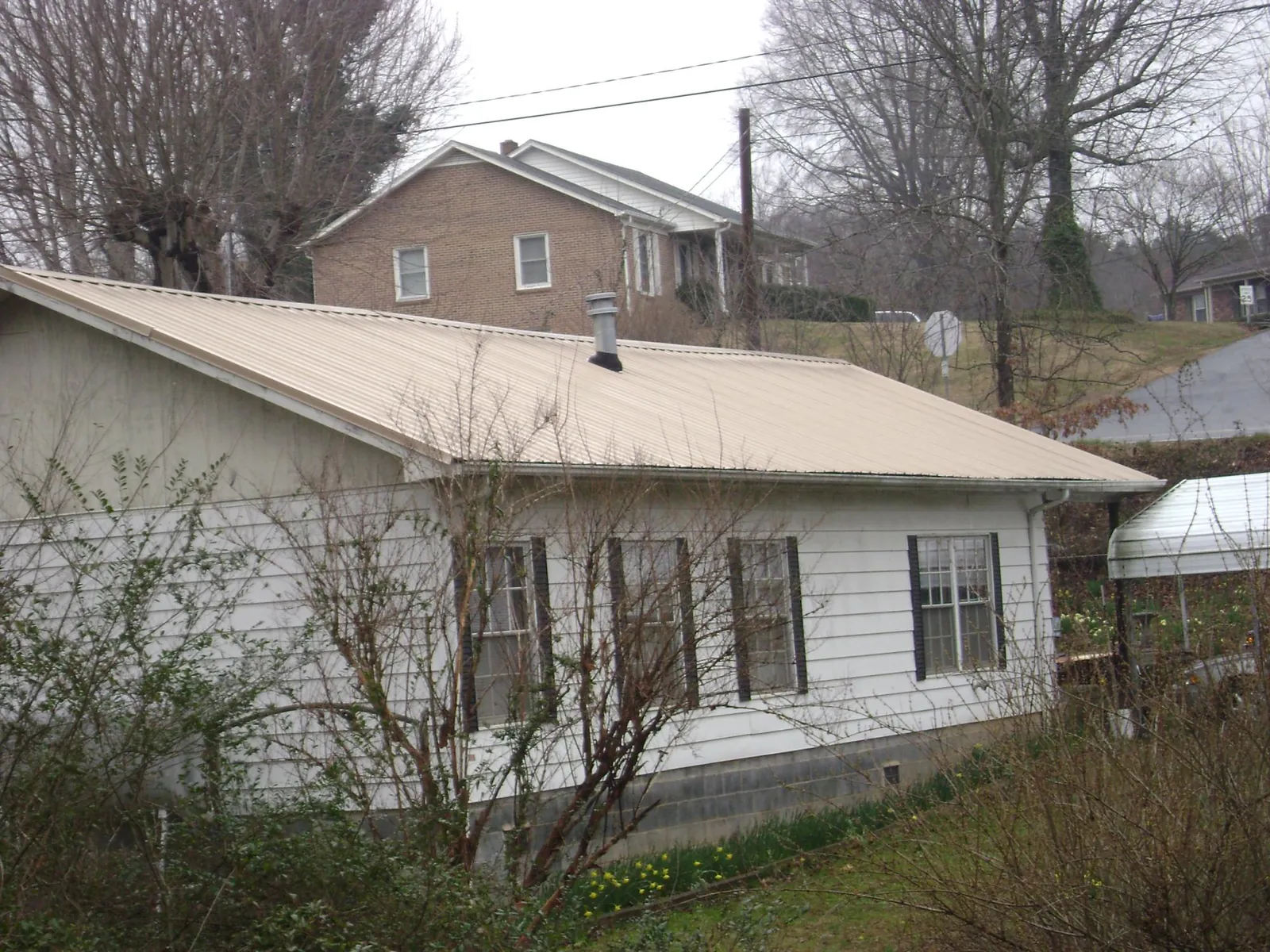 Tan metal roof on a white sided house set into a hillside — Commercial Roofing by Roofing Brothers in Milmay